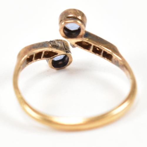 114 - An 18ct gold, sapphire and diamond cross over ring. The ring having two bezel set round cut sapphire... 