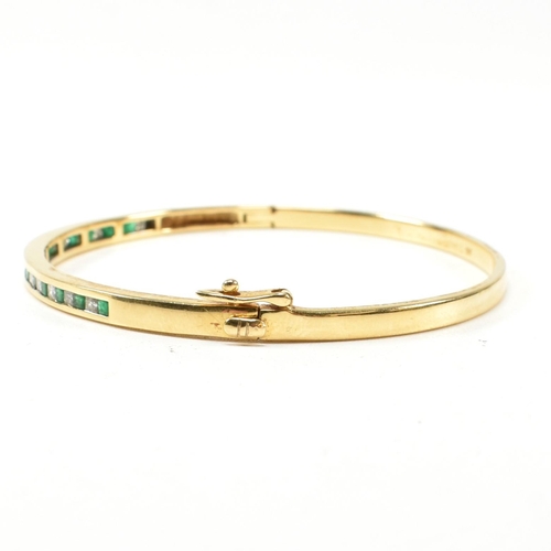 148 - An 18ct gold, emerald and diamond hinged bangle. The bangle having fifteen channel set princess cut ... 