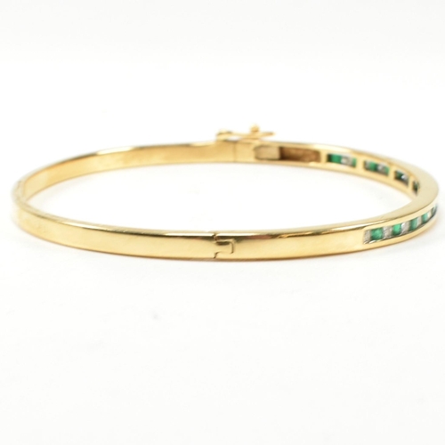 148 - An 18ct gold, emerald and diamond hinged bangle. The bangle having fifteen channel set princess cut ... 