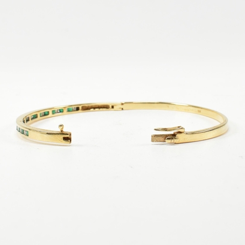 148 - An 18ct gold, emerald and diamond hinged bangle. The bangle having fifteen channel set princess cut ... 