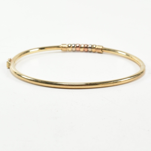 182 - A hallmarked 9ct gold hinged bangle. The gold hinged bangle having a tri-colour ring design to box c... 