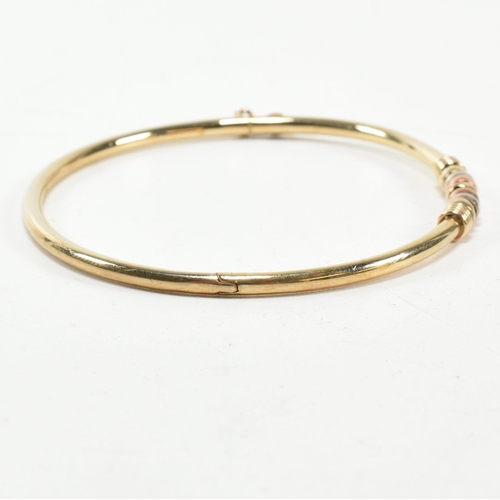 182 - A hallmarked 9ct gold hinged bangle. The gold hinged bangle having a tri-colour ring design to box c... 