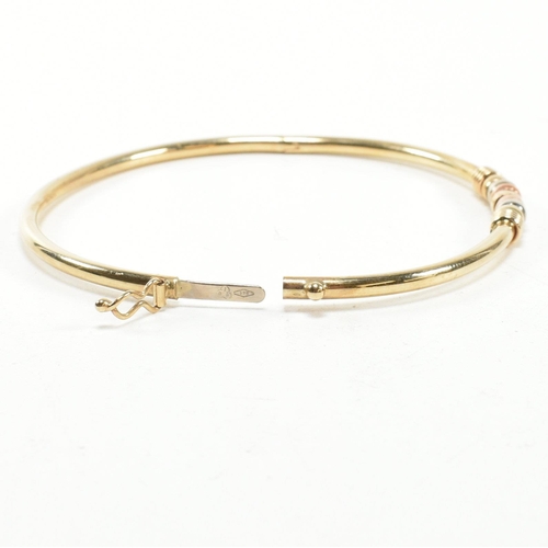 182 - A hallmarked 9ct gold hinged bangle. The gold hinged bangle having a tri-colour ring design to box c... 