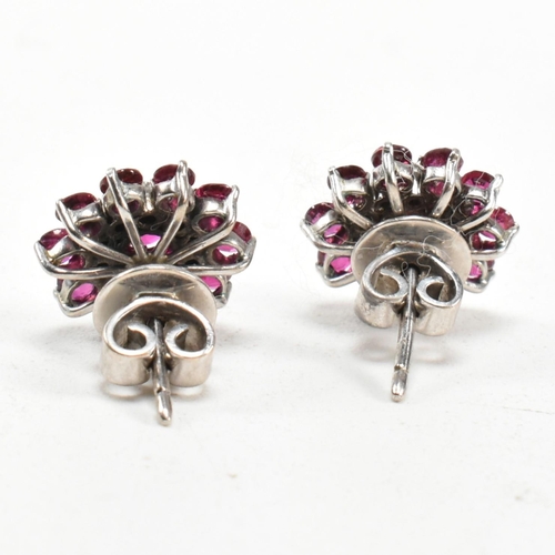 238 - A pair of white gold ruby and diamond cluster earrings. The earrings set set with round cut rubies a... 