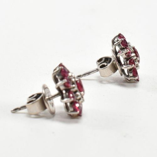 238 - A pair of white gold ruby and diamond cluster earrings. The earrings set set with round cut rubies a... 