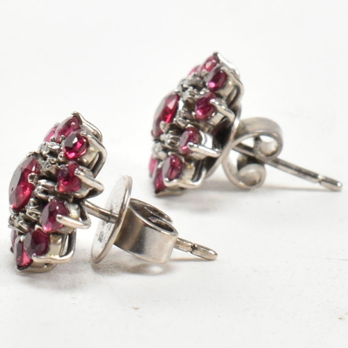 238 - A pair of white gold ruby and diamond cluster earrings. The earrings set set with round cut rubies a... 