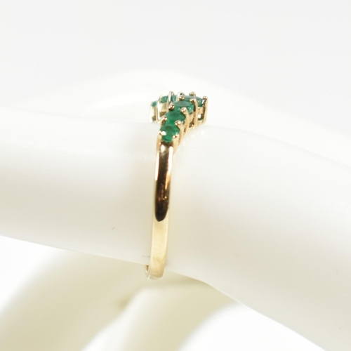 292 - A hallmarked 9ct gold and emerald wishbone ring. The ring set with a single row of shared claw round... 