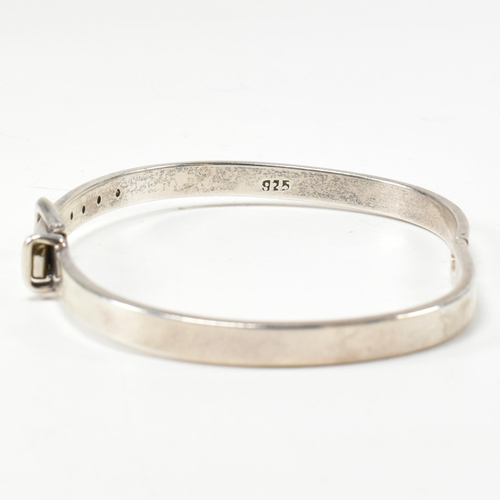 395 - A hallmarked silver belt buckle hinged bangle. The silver belt bangle having a central belt buckle c... 