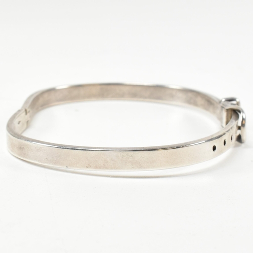 395 - A hallmarked silver belt buckle hinged bangle. The silver belt bangle having a central belt buckle c... 