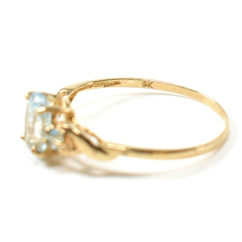 400 - A 9ct gold and blue topaz ring. The ring set with a central oval cut topaz flanked by two round cut ... 