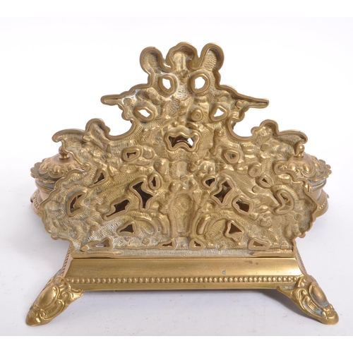 255 - A 20th century brass rococo manner inkwell desk tidy. The desk tidy raised on four feet, with matchi... 