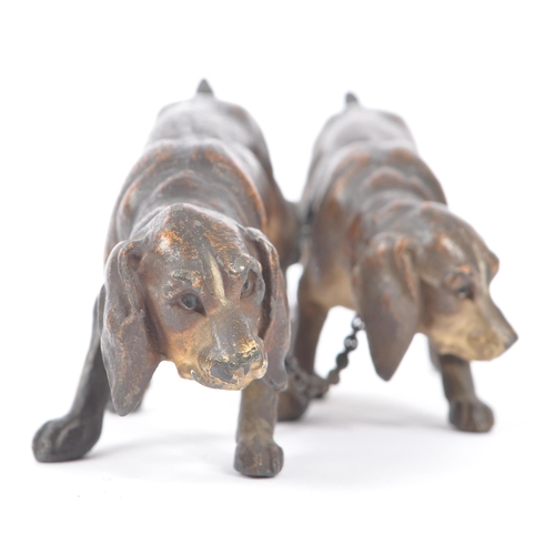 314 - A hollow bronze figurine in the form of two dogs / hounds attached together by chain, both standing ... 