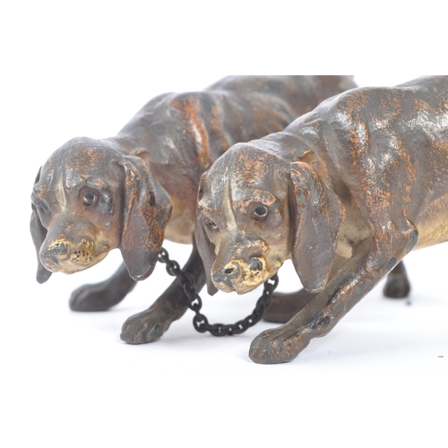 314 - A hollow bronze figurine in the form of two dogs / hounds attached together by chain, both standing ... 