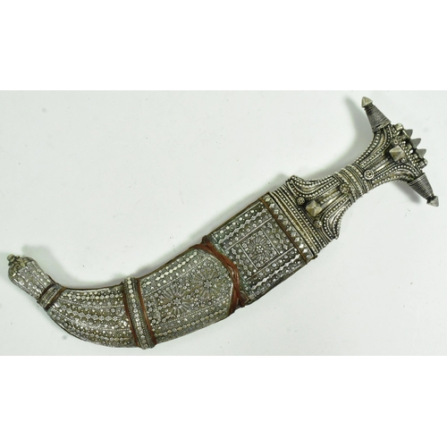 31 - An early 20th Century Saudi Arabian Jambiya / Khanjar dagger. Ornate hilt with applied silver orname... 