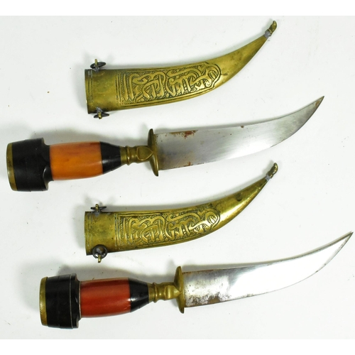 318 - A pair of Syrian Jambiya daggers with brass floral motif pommels, layered man made grips inlaid with... 