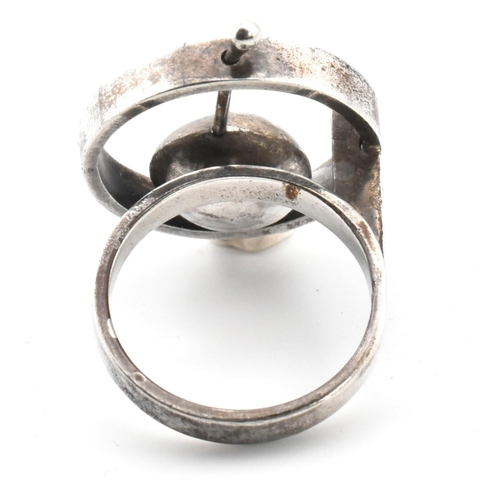 24 - A mid-century modernist 800 silver ring. The ring having a roundel top with articulating cup to plai... 