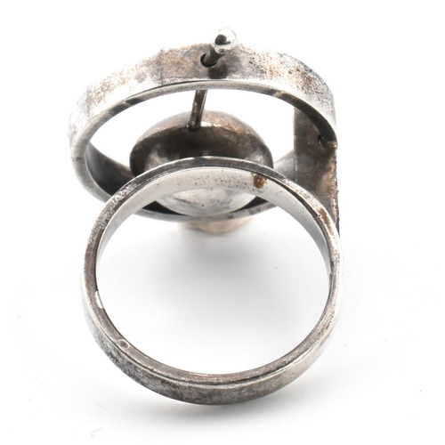 24 - A mid-century modernist 800 silver ring. The ring having a roundel top with articulating cup to plai... 