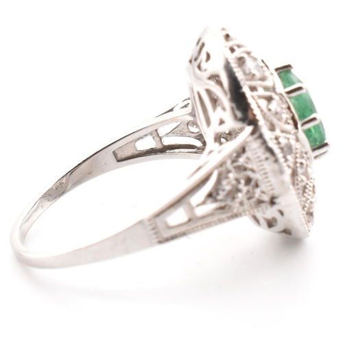 50 - A 18ct white gold emerald and diamond cluster ring. The ring set with an oval cut emerald to a pierc... 