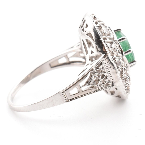 50 - A 18ct white gold emerald and diamond cluster ring. The ring set with an oval cut emerald to a pierc... 