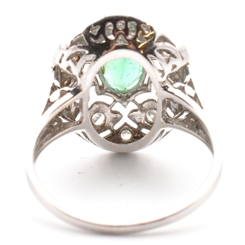 50 - A 18ct white gold emerald and diamond cluster ring. The ring set with an oval cut emerald to a pierc... 