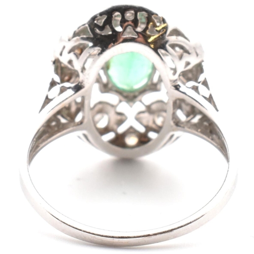 50 - A 18ct white gold emerald and diamond cluster ring. The ring set with an oval cut emerald to a pierc... 