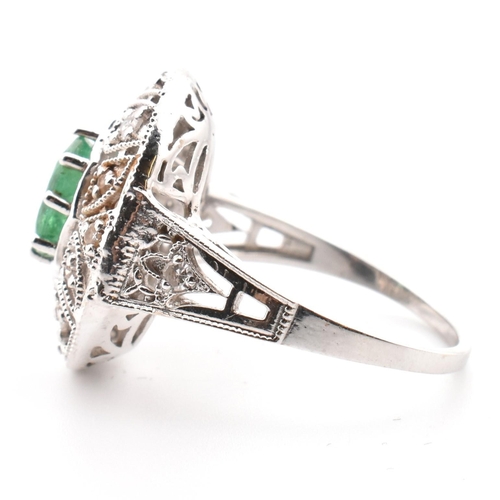 50 - A 18ct white gold emerald and diamond cluster ring. The ring set with an oval cut emerald to a pierc... 