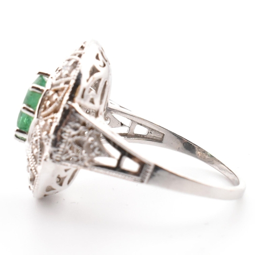 50 - A 18ct white gold emerald and diamond cluster ring. The ring set with an oval cut emerald to a pierc... 