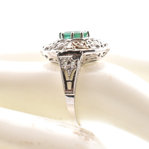 50 - A 18ct white gold emerald and diamond cluster ring. The ring set with an oval cut emerald to a pierc... 