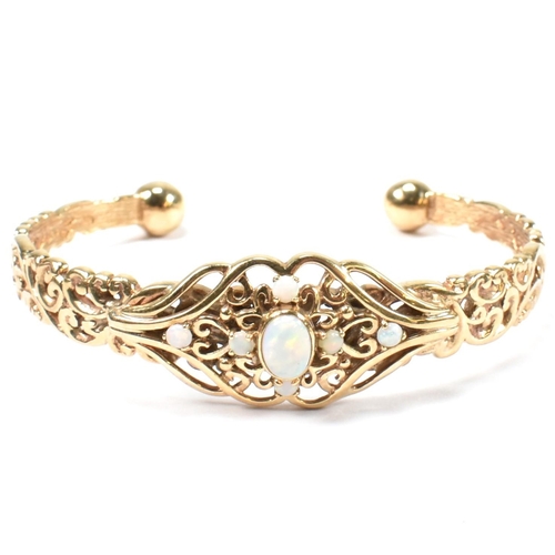 73 - A hallmarked 9ct gold and opal torque bangle. The yellow gold bangle having pierced scrolling decora... 