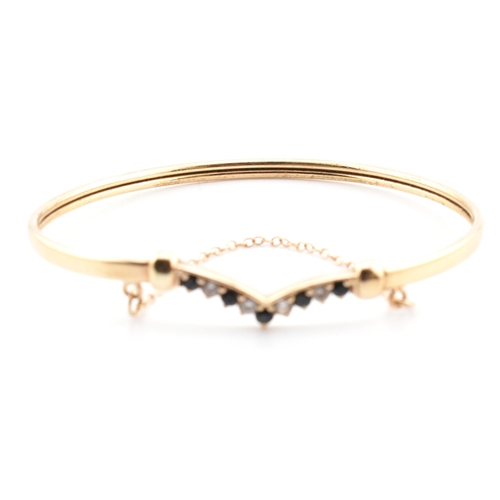 78 - A hallmarked 9ct gold, CZ and sapphire wishbone bangle. The 9ct gold bangle wishbone bangle having a... 