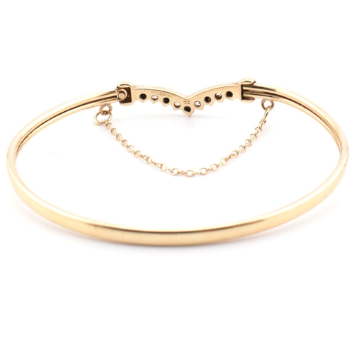 78 - A hallmarked 9ct gold, CZ and sapphire wishbone bangle. The 9ct gold bangle wishbone bangle having a... 