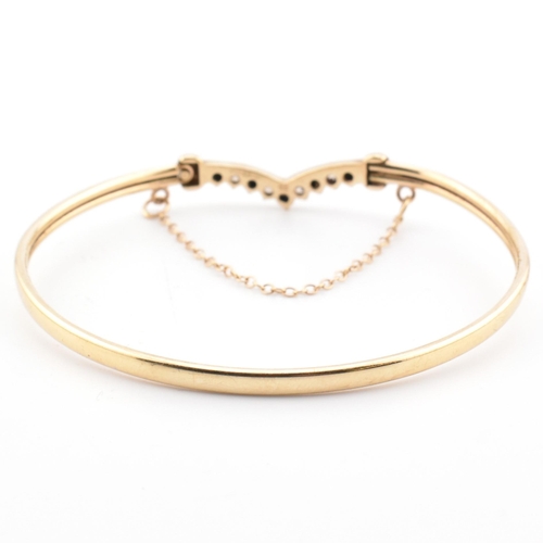 78 - A hallmarked 9ct gold, CZ and sapphire wishbone bangle. The 9ct gold bangle wishbone bangle having a... 