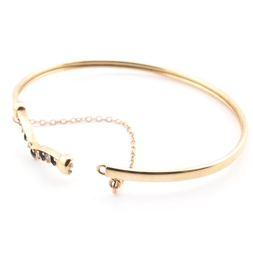 78 - A hallmarked 9ct gold, CZ and sapphire wishbone bangle. The 9ct gold bangle wishbone bangle having a... 