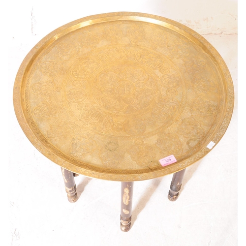 939 - A 20th Century Indian Benares folding side table. The table having brass tray charger to top with en... 