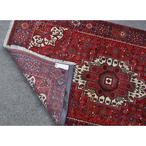 1042 - A mid 20th century Persian Goltuk hand knotted carpet floor rug. The rug having a red ground with la... 