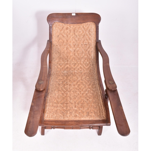 415 - An early 20th century plantation teak & wicker rattan seat lounge chair. The chair having a reclined... 