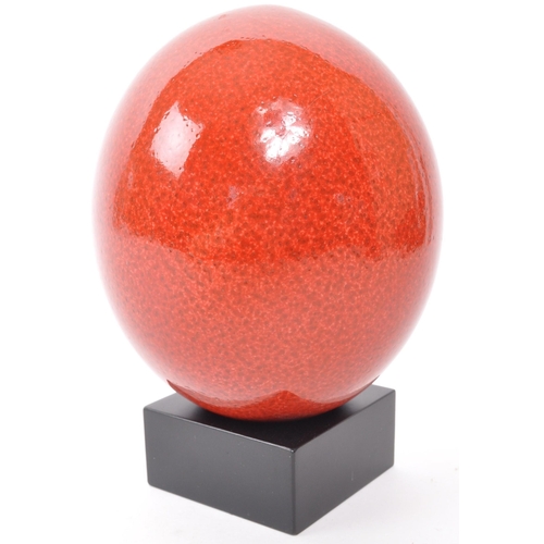 202 - A 20th Century sanguine colour ostrich egg raised upon square black base. Measuring approximately 18... 