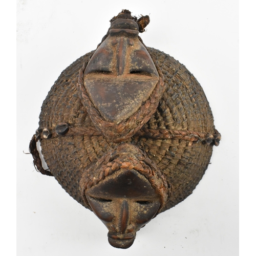 86 - An African tribal straw helmet hat. The dome shaped straw hat decorated with two wooden carved faces... 