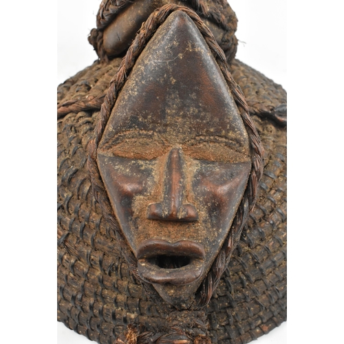 86 - An African tribal straw helmet hat. The dome shaped straw hat decorated with two wooden carved faces... 