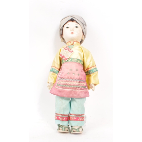 222 - A vintage 1950s Chinese doll, with hard plastic head and hands, dressed in pink, yellow and blue tra... 