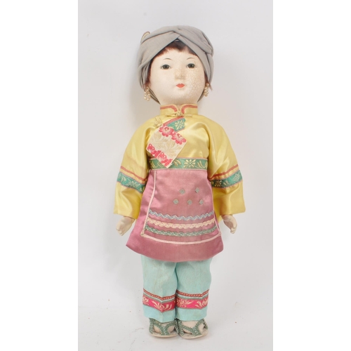 222 - A vintage 1950s Chinese doll, with hard plastic head and hands, dressed in pink, yellow and blue tra... 