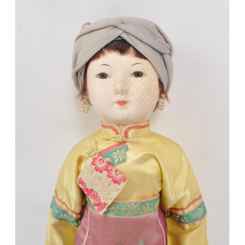 222 - A vintage 1950s Chinese doll, with hard plastic head and hands, dressed in pink, yellow and blue tra... 