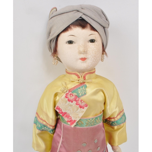 222 - A vintage 1950s Chinese doll, with hard plastic head and hands, dressed in pink, yellow and blue tra... 