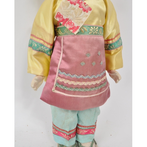 222 - A vintage 1950s Chinese doll, with hard plastic head and hands, dressed in pink, yellow and blue tra... 