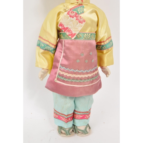 222 - A vintage 1950s Chinese doll, with hard plastic head and hands, dressed in pink, yellow and blue tra... 