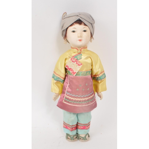 222 - A vintage 1950s Chinese doll, with hard plastic head and hands, dressed in pink, yellow and blue tra... 