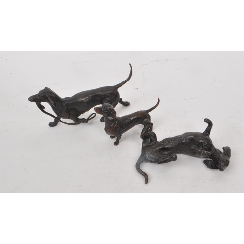 229 - Richard Cooper - Three contemporary bronze Dachshund dog figures, comprising of a dog rolling over, ... 