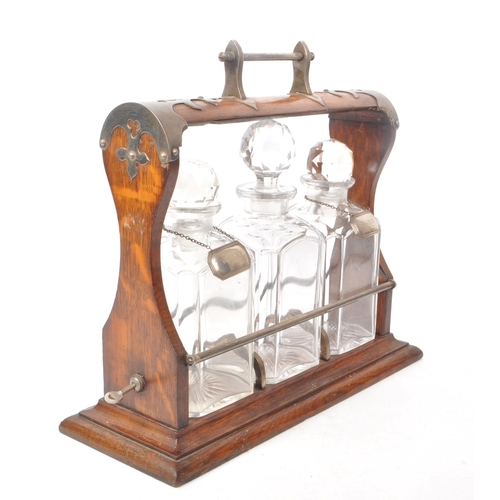 254 - A wooden early 20th/ 19th century tantalus with metal detailing. Comes with three cut glass decanter... 