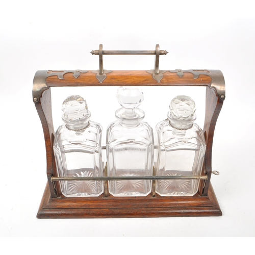 254 - A wooden early 20th/ 19th century tantalus with metal detailing. Comes with three cut glass decanter... 