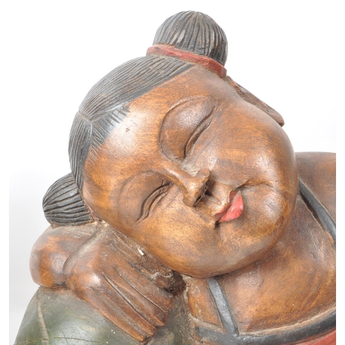 208 - A pair of vintage 20th-century Chinese wooden reclining figures, both dressed in a black and red out... 